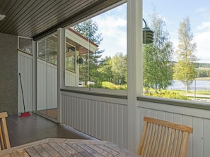 A covered outdoor area with a table and chairs, a broom, and a view of a lake and trees.