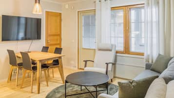 Ein modernes Wohnzimmer mit einem Holzesstisch, Stühlen, einer Couch, einem runden Couchtisch und einem an der Wand montierten Fernseher.