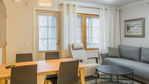 Ein modernes Wohnzimmer mit einem Holzespeisetisch, zwei Stühlen, einem grauen Sofa, einem kleinen runden Tisch und einem Gemälde an der Wand.