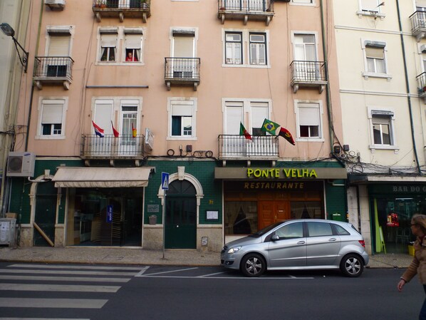 A building with multiple balconies, a restaurant named 'Ponte Velha' on the ground floor, and a silver car parked in front. - Hospedaria D. Damélio (Lisbon)