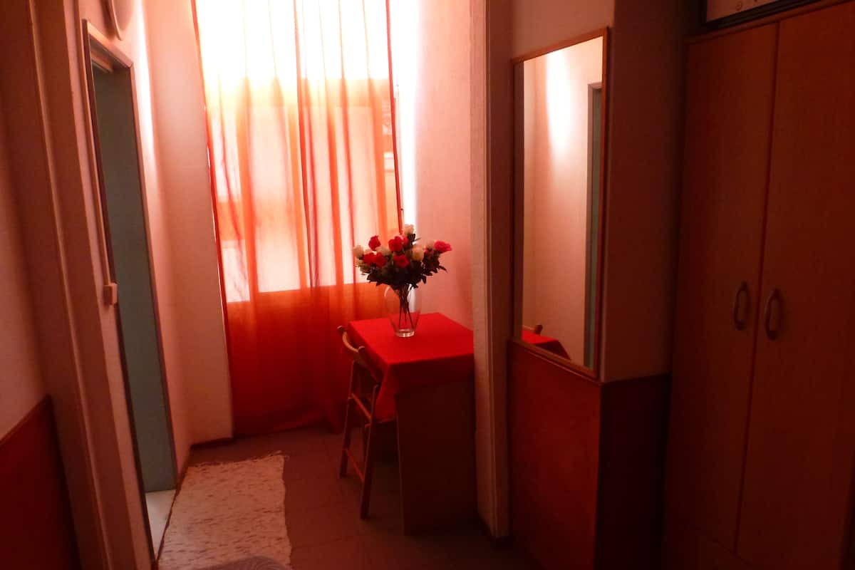 Ein kleiner Raum mit einem roten Tisch, einem Stuhl, einer Blumenvase, einem Spiegel und einem Kleiderschrank.