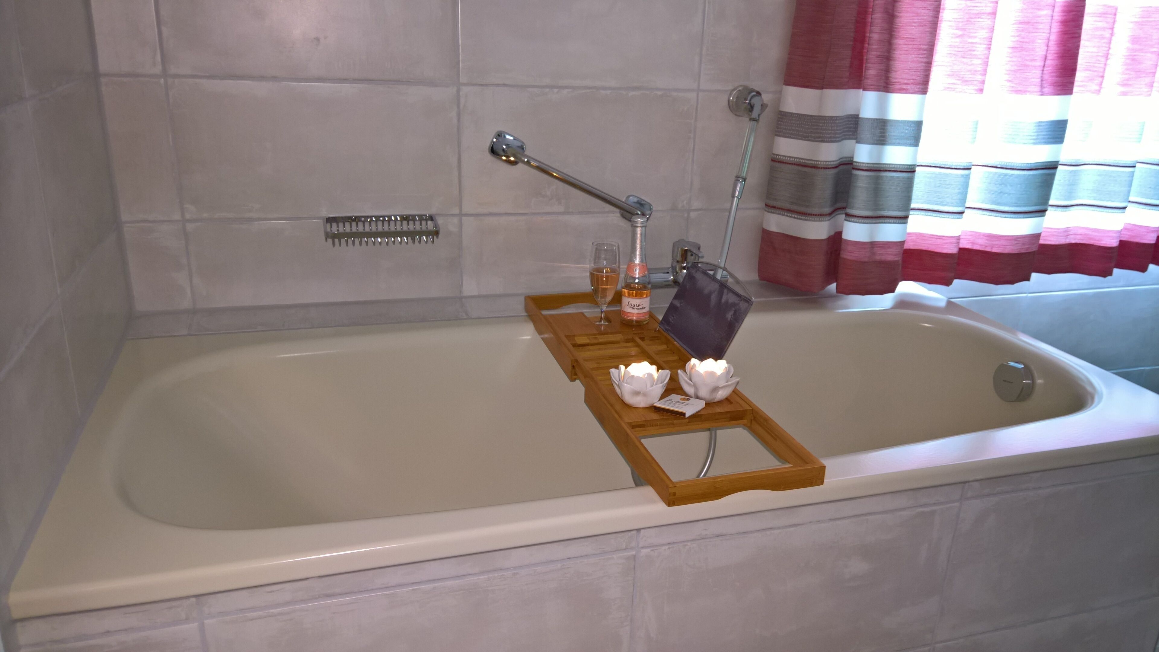 Une salle de bain avec une baignoire, une douche, un plateau en bois avec des bougies, une bouteille de vin et un verre.