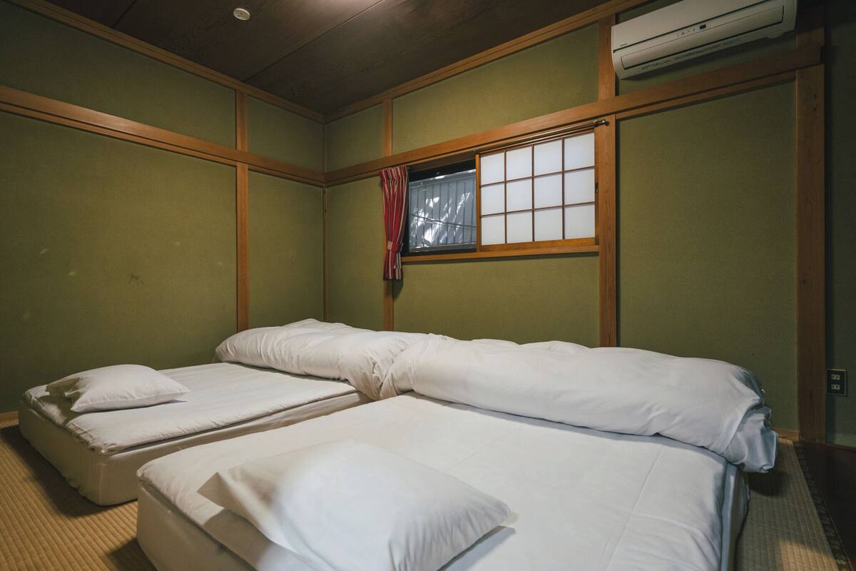 Una habitación con dos camas, una ventana con cortina e instalación de aire acondicionado.