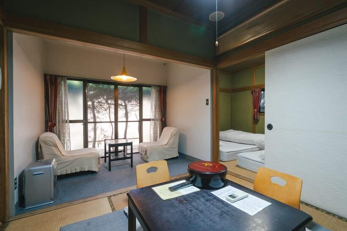 Una habitación con sofá, una mesa de comedor, una mesita con un objeto rojo y una ventana con cortinas.