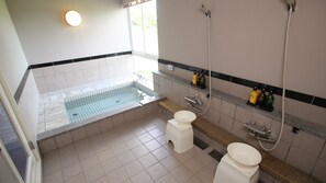 Een moderne badkamer met een bad, twee toiletten, een wastafel en een douche.