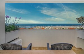Una terraza con vista a una playa y al océano, dos sillas y una mesa.