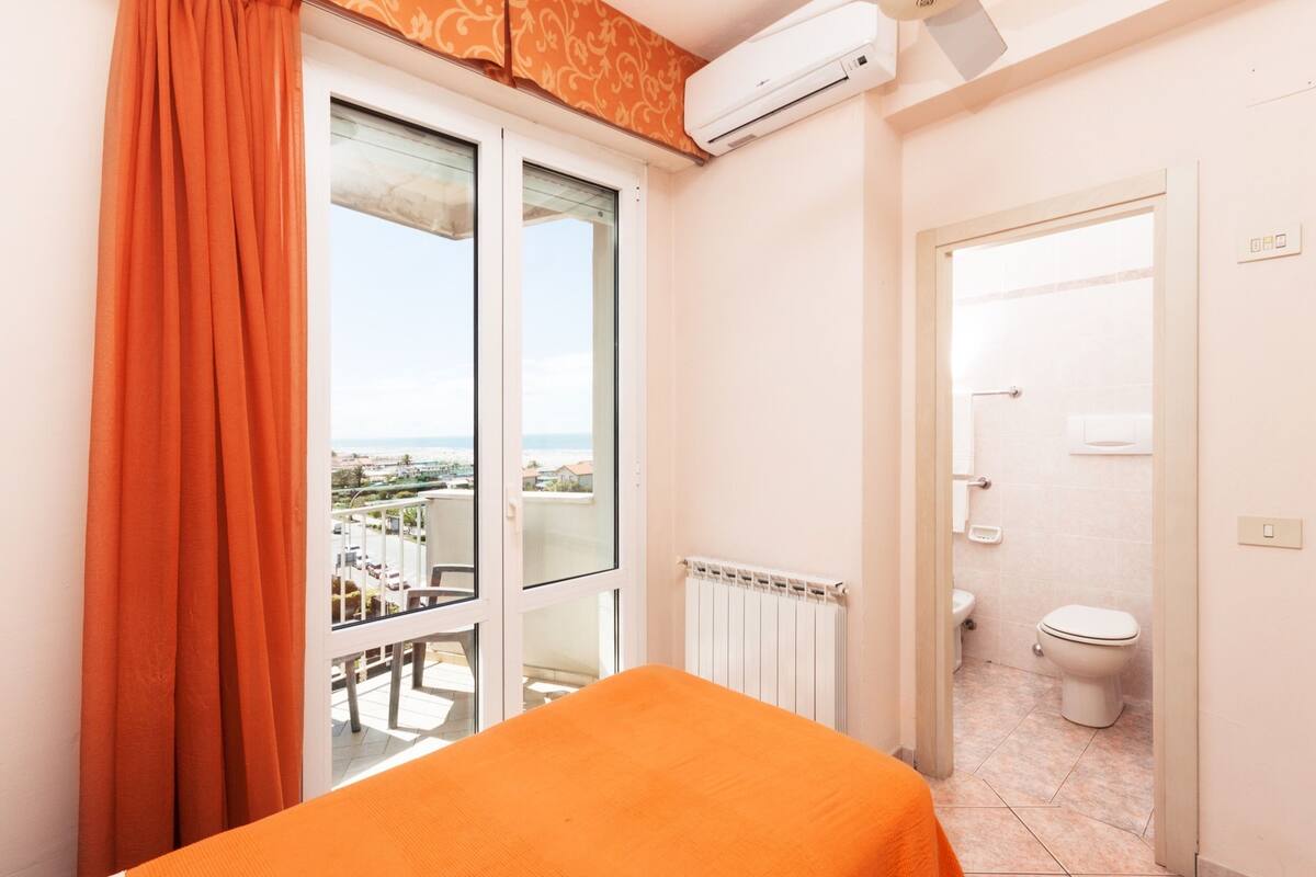Quarto de hotel com varanda, vista da cidade, banheiro com vaso sanitário e pia, e ar condicionado.