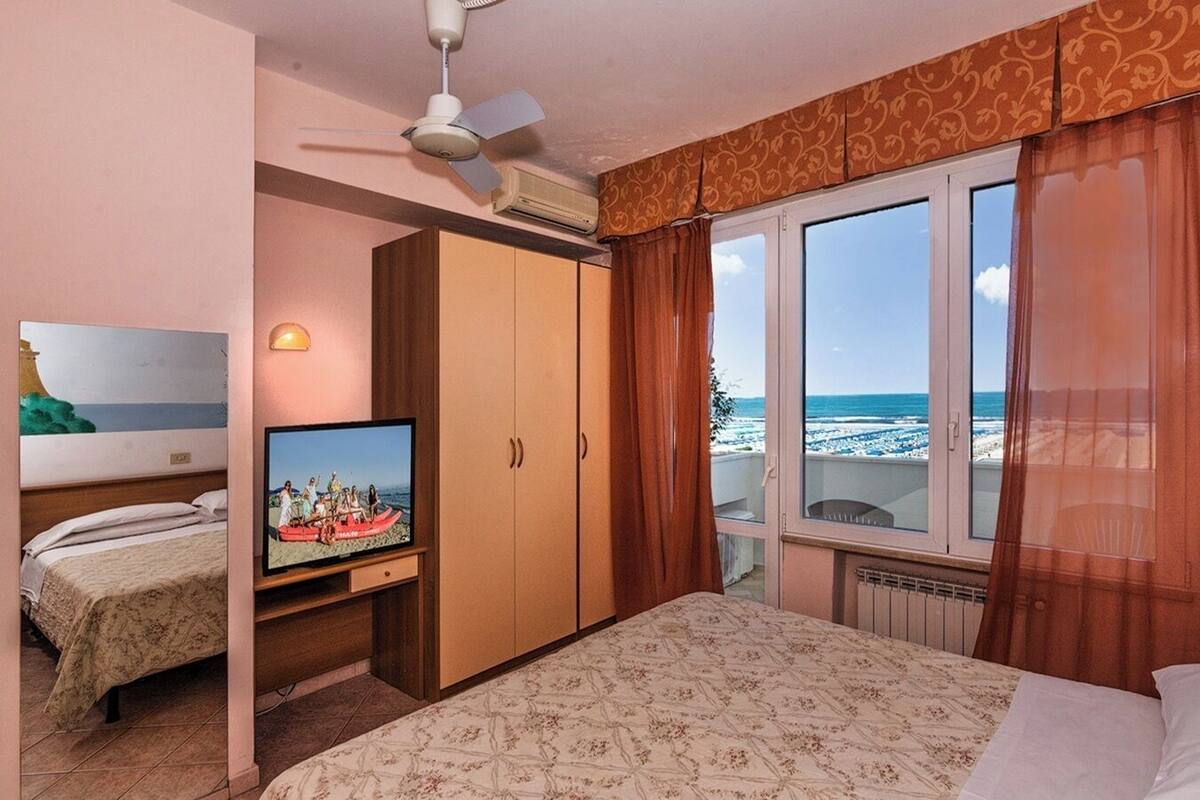 Quarto com cama, televisão, guarda-roupa e janela com vista para a praia.