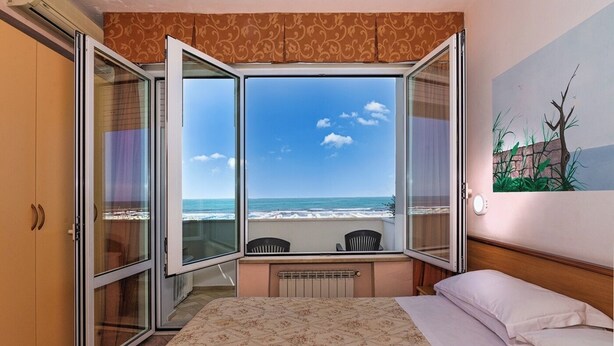 A hotel room with a bed, a desk, and a view of the beach. - Hotel Ambasciatori (Pietrasanta)