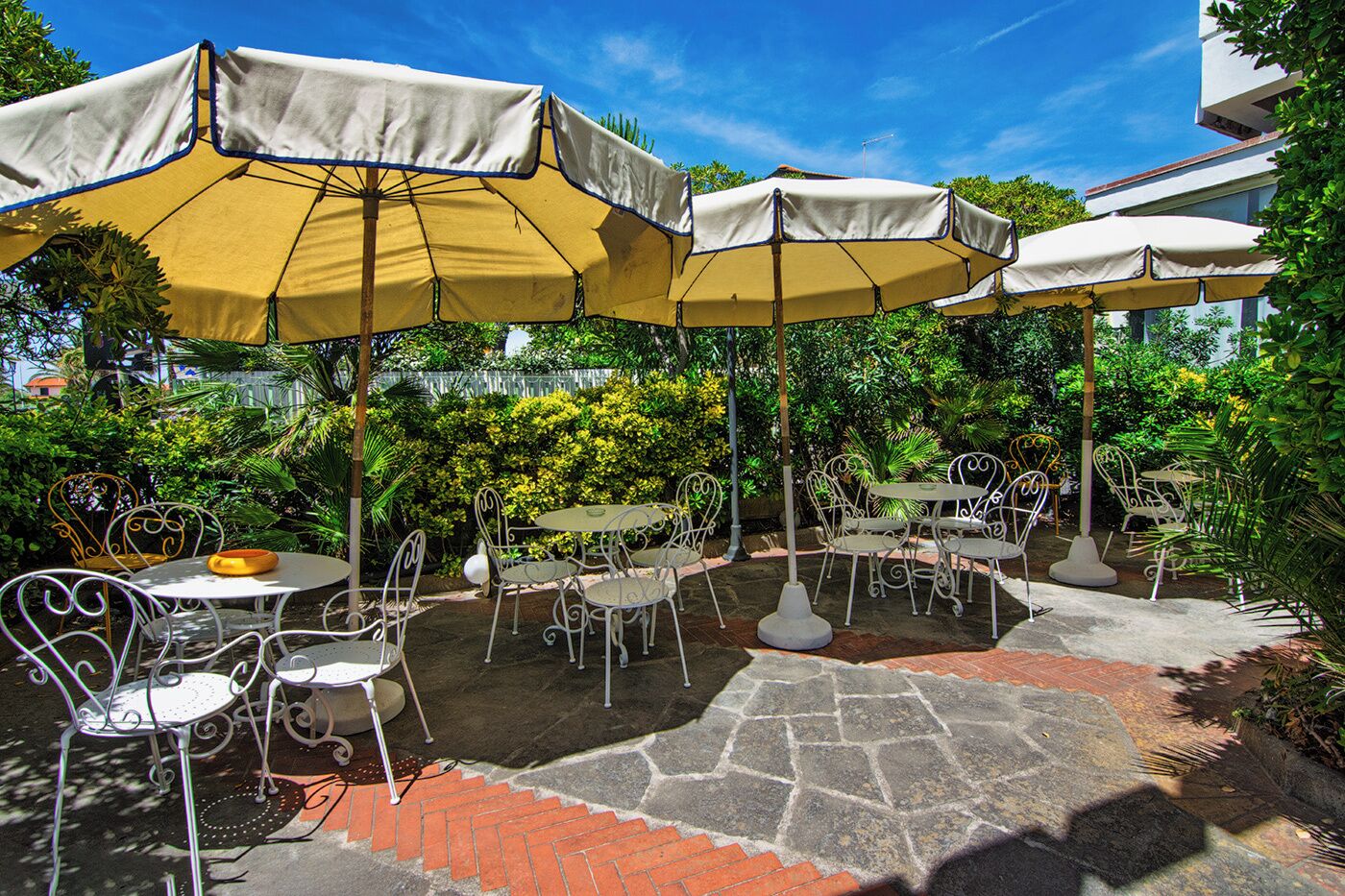 Un patio al aire libre con piso de piedra, sillas y mesas de metal y sombrillas amarillas.