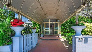 A covered entrance with a white picket fence, potted plants, and a brick pathway leading to a glass door. - Hotel Ambasciatori (Pietrasanta)
