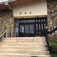 Entrada de un edificio con fachada de piedra, unos escalones que conducen a una puerta de color oscuro y un cartel sobre la puerta.
