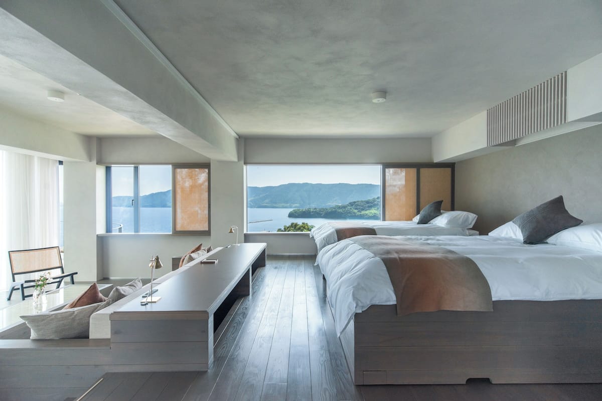 A modern bedroom with a large bed, a desk, and a view of the sea.