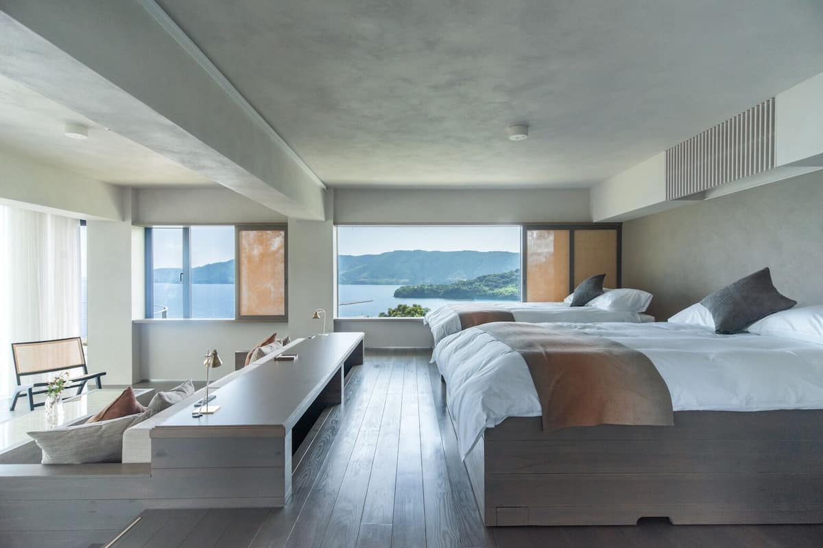 A modern hotel room with a large bed, a desk, and a view of the sea.