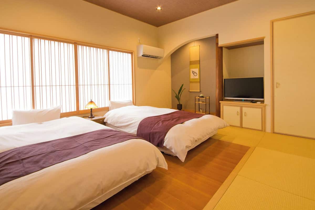 A hotel room with two beds, a TV, a wardrobe, and a window with blinds.