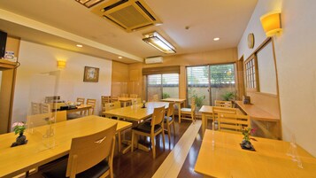 Un comedor con mesas y sillas de madera, un ventanal con persianas y un equipo de aire acondicionado en el techo.