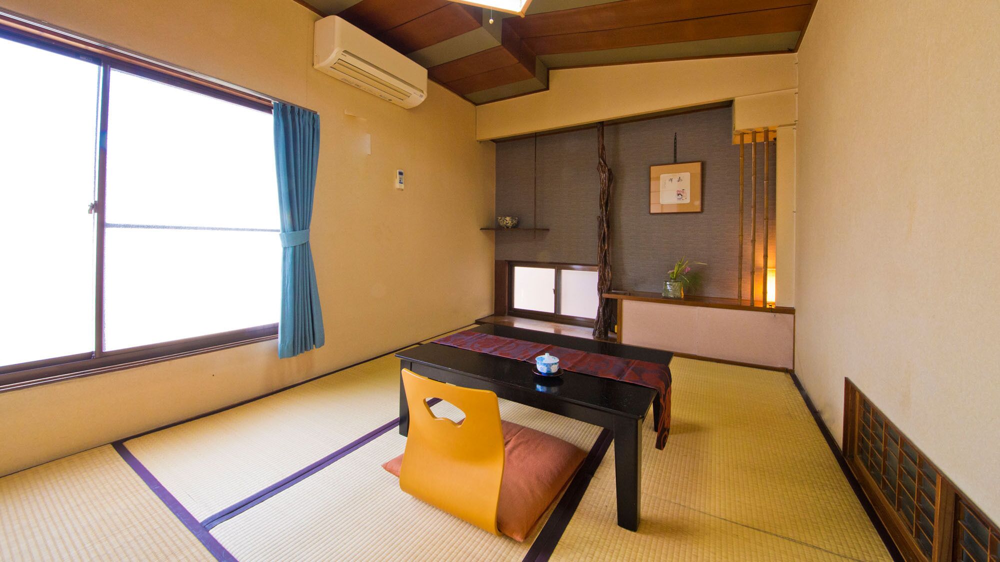 A traditional Japanese room with tatami flooring, a low table, a yellow chair, a sliding door, and a small shelf with decorative items.