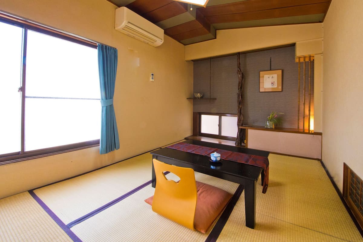 A traditional Japanese room with tatami flooring, a low table, a yellow chair, a sliding door, and a small shelf with decorative items.