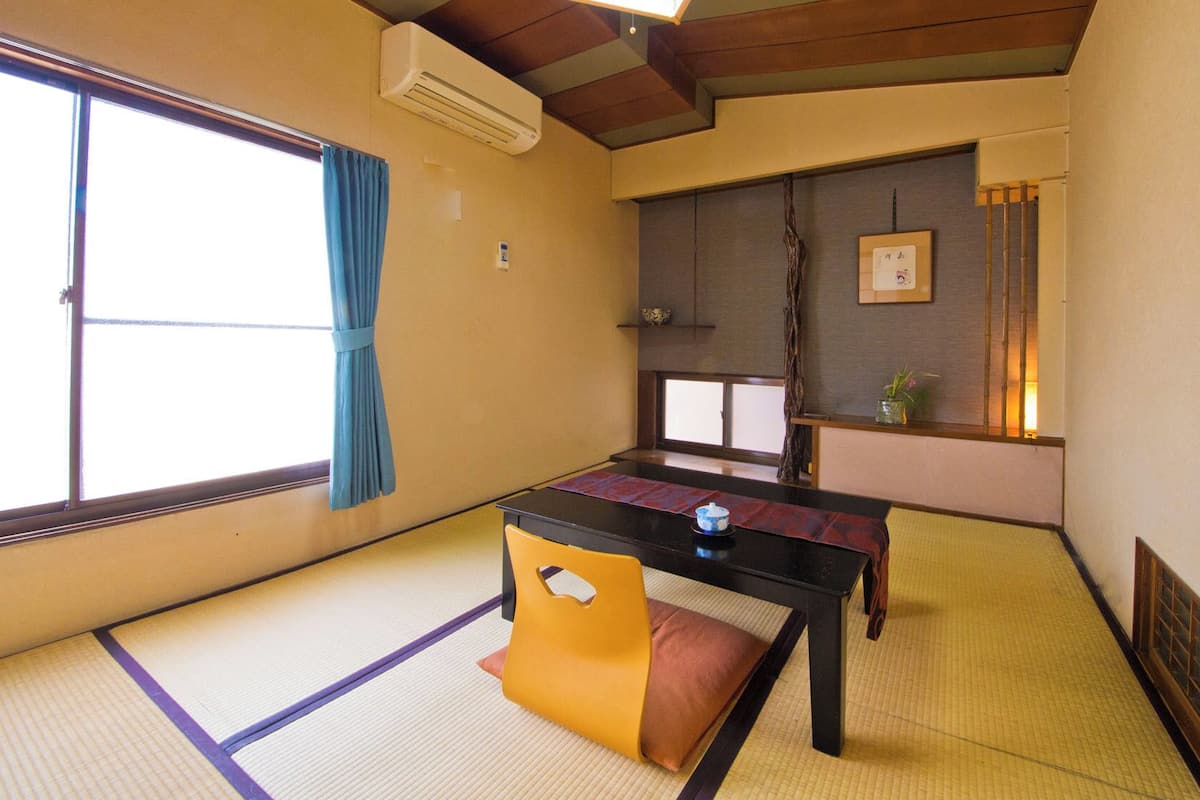 A traditional Japanese room with tatami flooring, a low table, a yellow chair, and a sliding door.