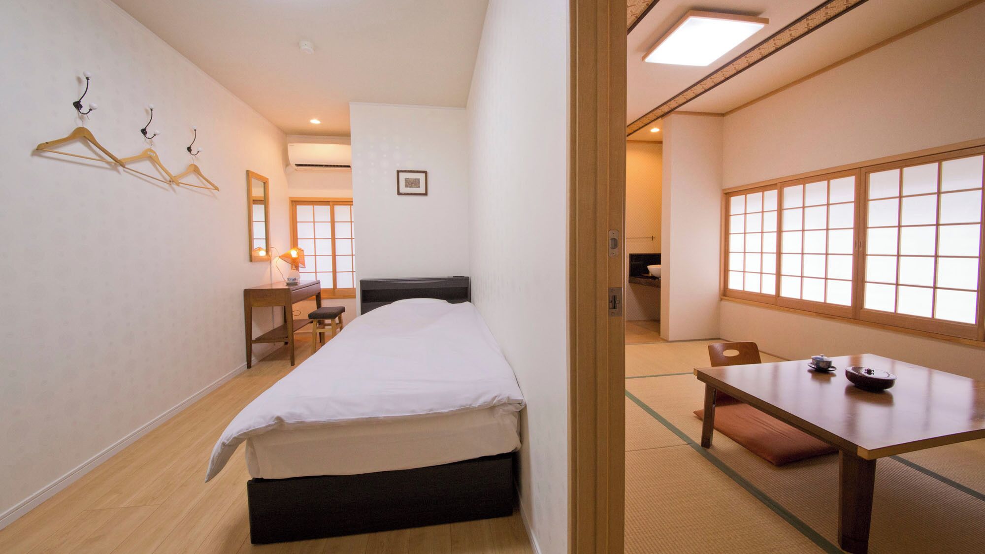 A hotel room with a bed, desk, chair, and a view through a shoji screen.