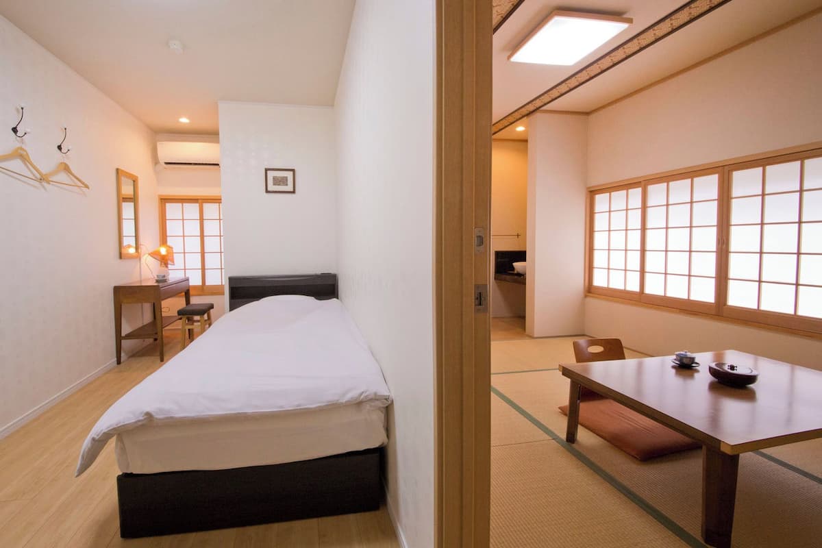 A hotel room with a bed, desk, chair, and a view through a shoji screen.