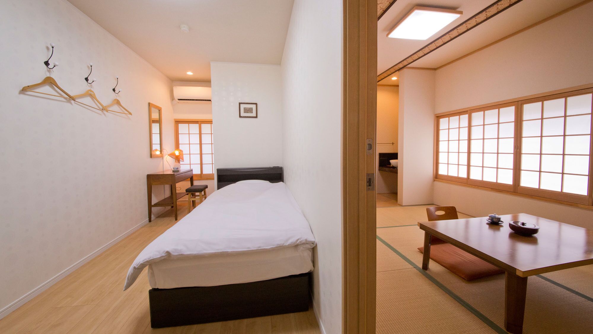 A hotel room with a bed, a desk, a chair, a table, and a view through a window.