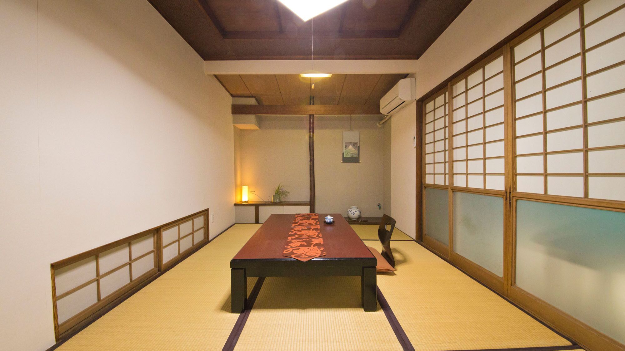 A tatami mat room with a low table, sliding doors, and a hanging light fixture.