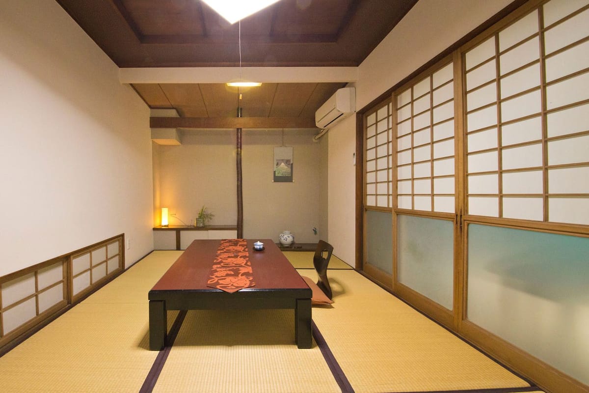 A tatami mat room with a low table, sliding doors, and a hanging light fixture.