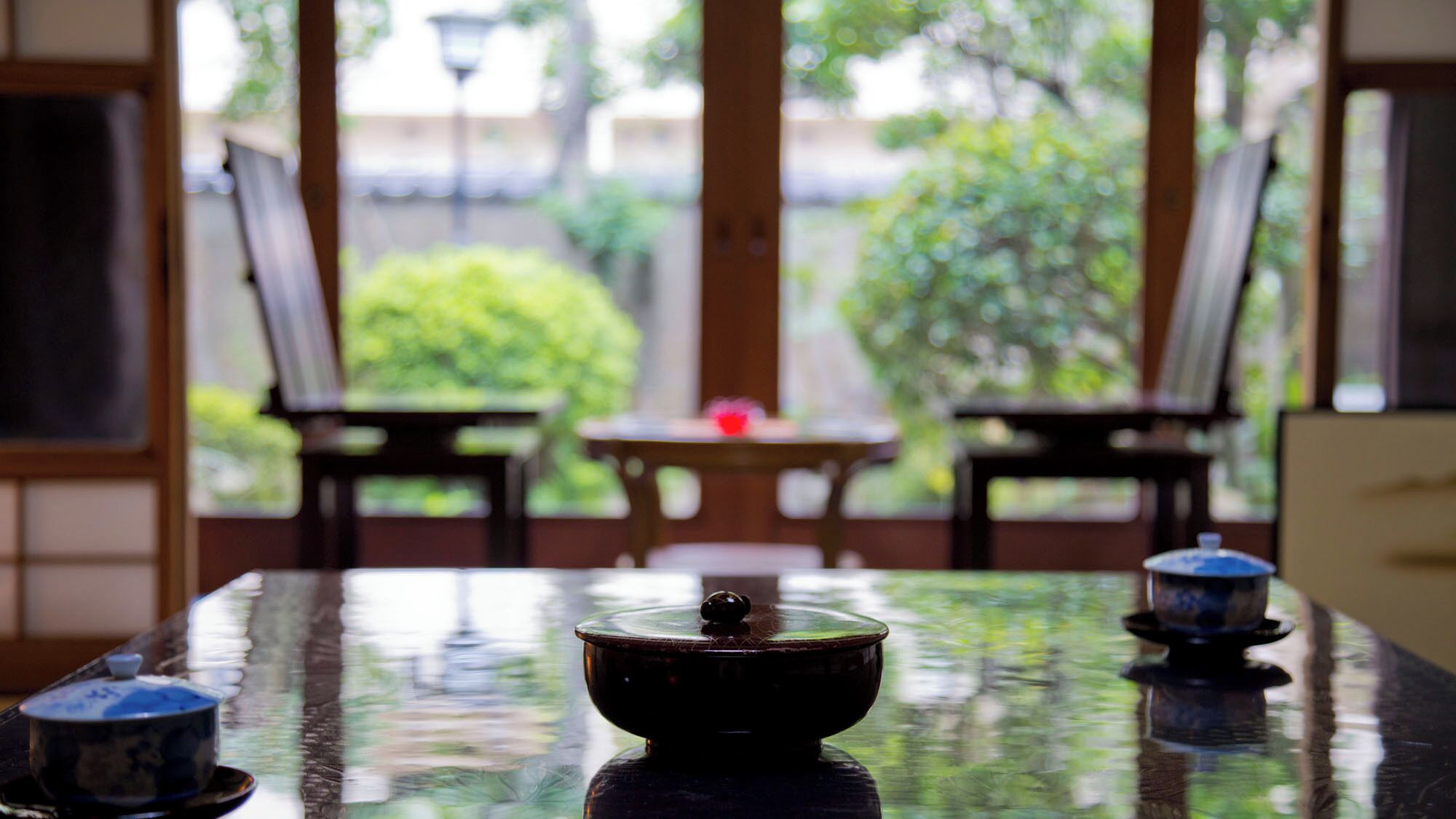 A table with a covered bowl in the center, flanked by two chairs and a small table with a red object on it.