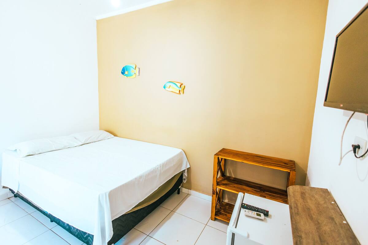 A room with a bed, a wooden nightstand, and two wall decorations.