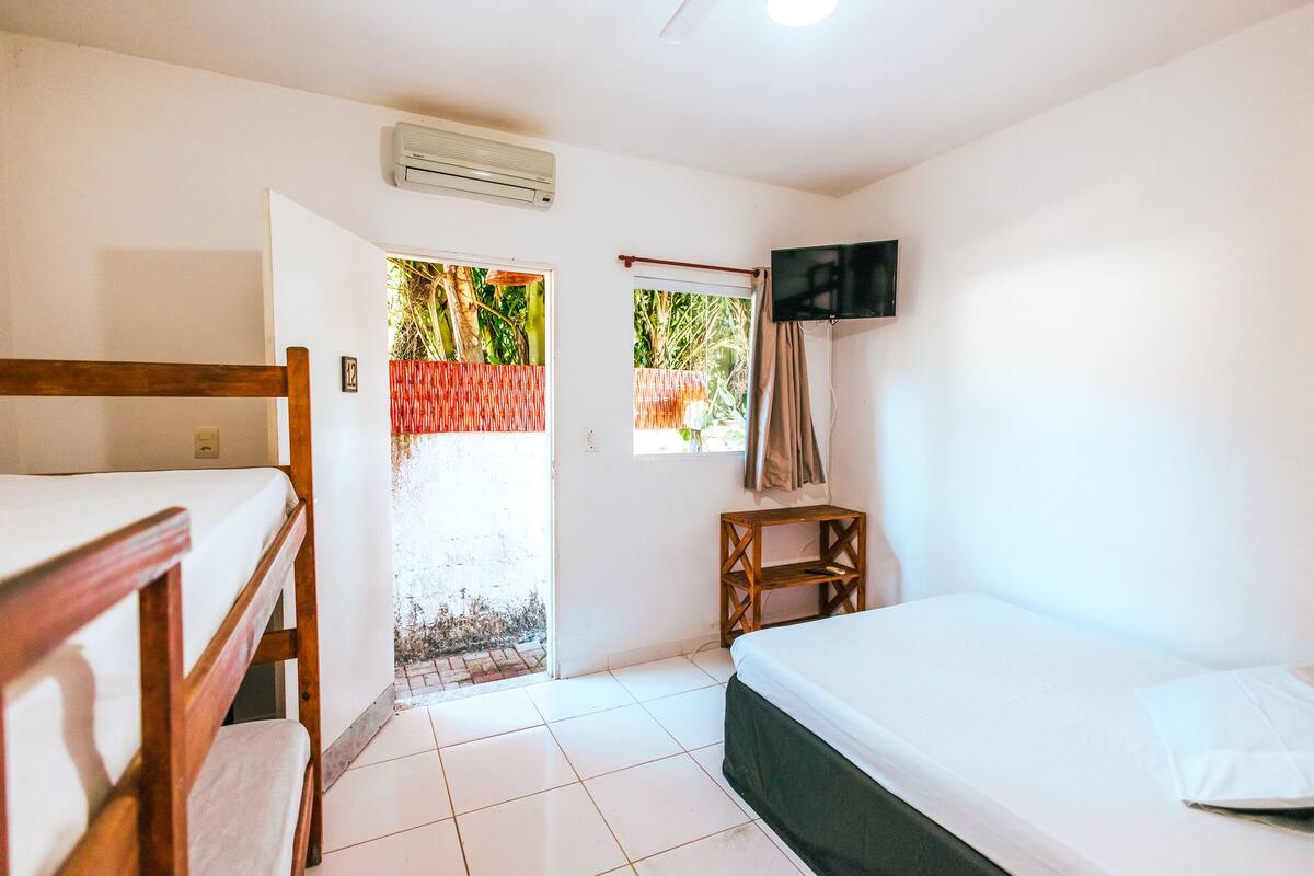 A room with bunk beds, a TV mounted on the wall, and a window with a view of greenery.