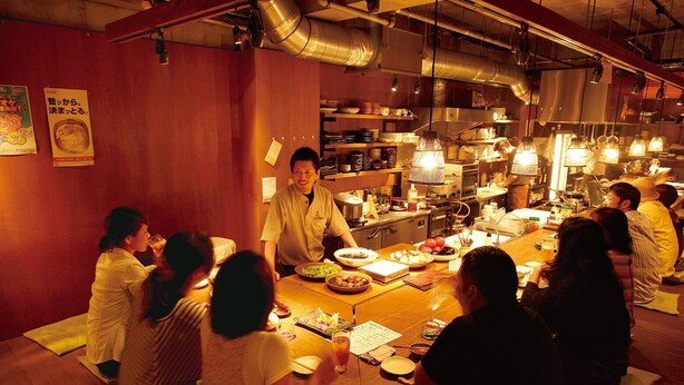 Ein traditionelles japanisches Restaurant mit Sitzgelegenheiten auf Tatami-Matten und einem Koch, der an der Theke Speisen zubereitet.