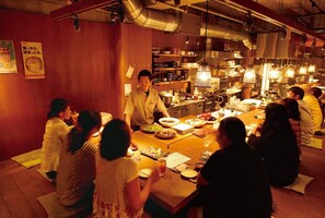 Een traditioneel Japans restaurant met tatami zitplaatsen en een kok die aan de bar gerechten bereidt.