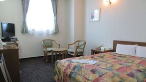Ein Hotelzimmer mit einem Bett, zwei Stühlen, einem Schreibtisch mit Fernseher und einem Nachttisch mit Lampe.
