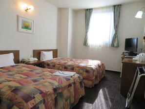 A hotel room with two beds, a desk with a computer, a telephone, and a television.