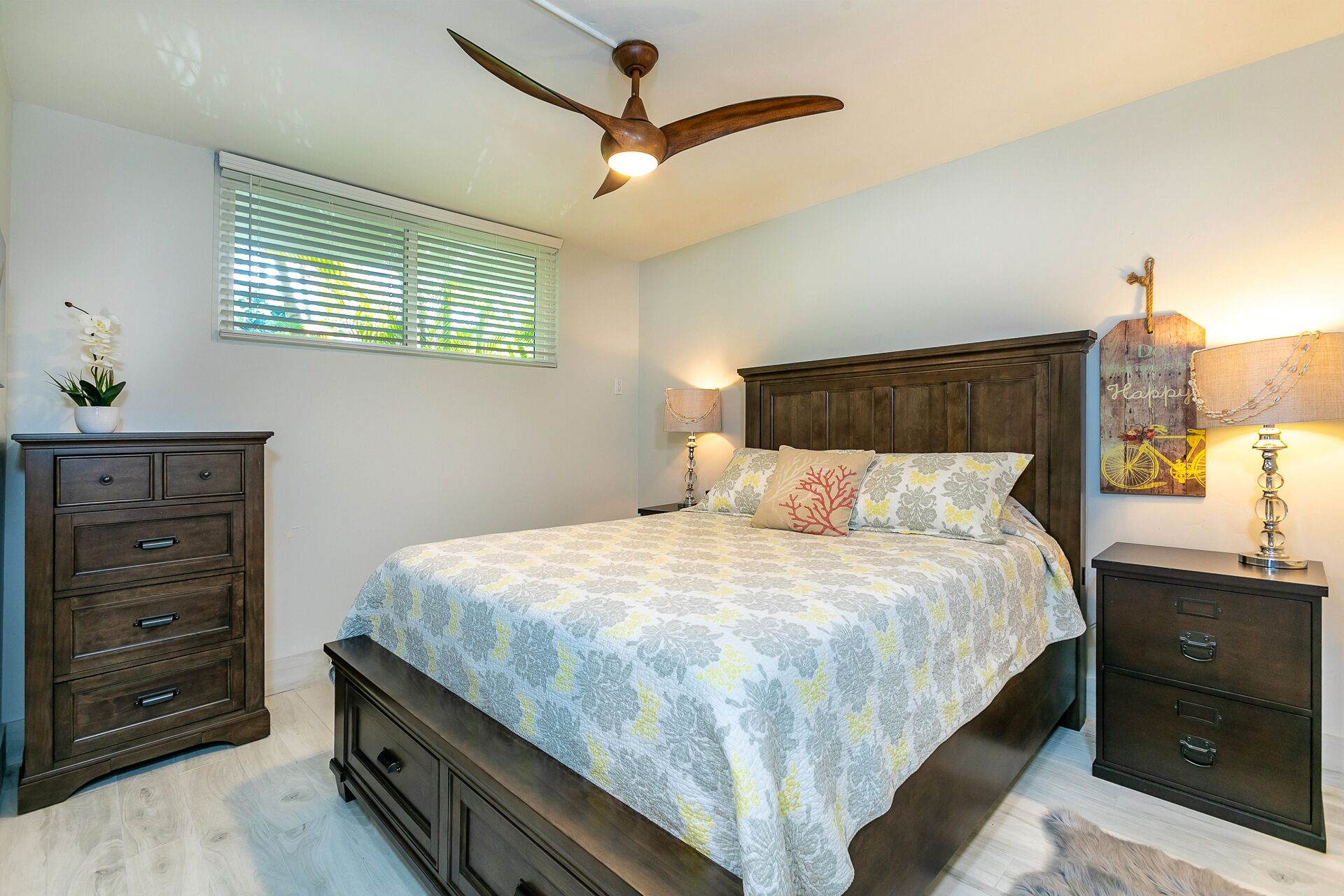 A bedroom with a wooden bed, a nightstand, a dresser, a ceiling fan, and a window with blinds.