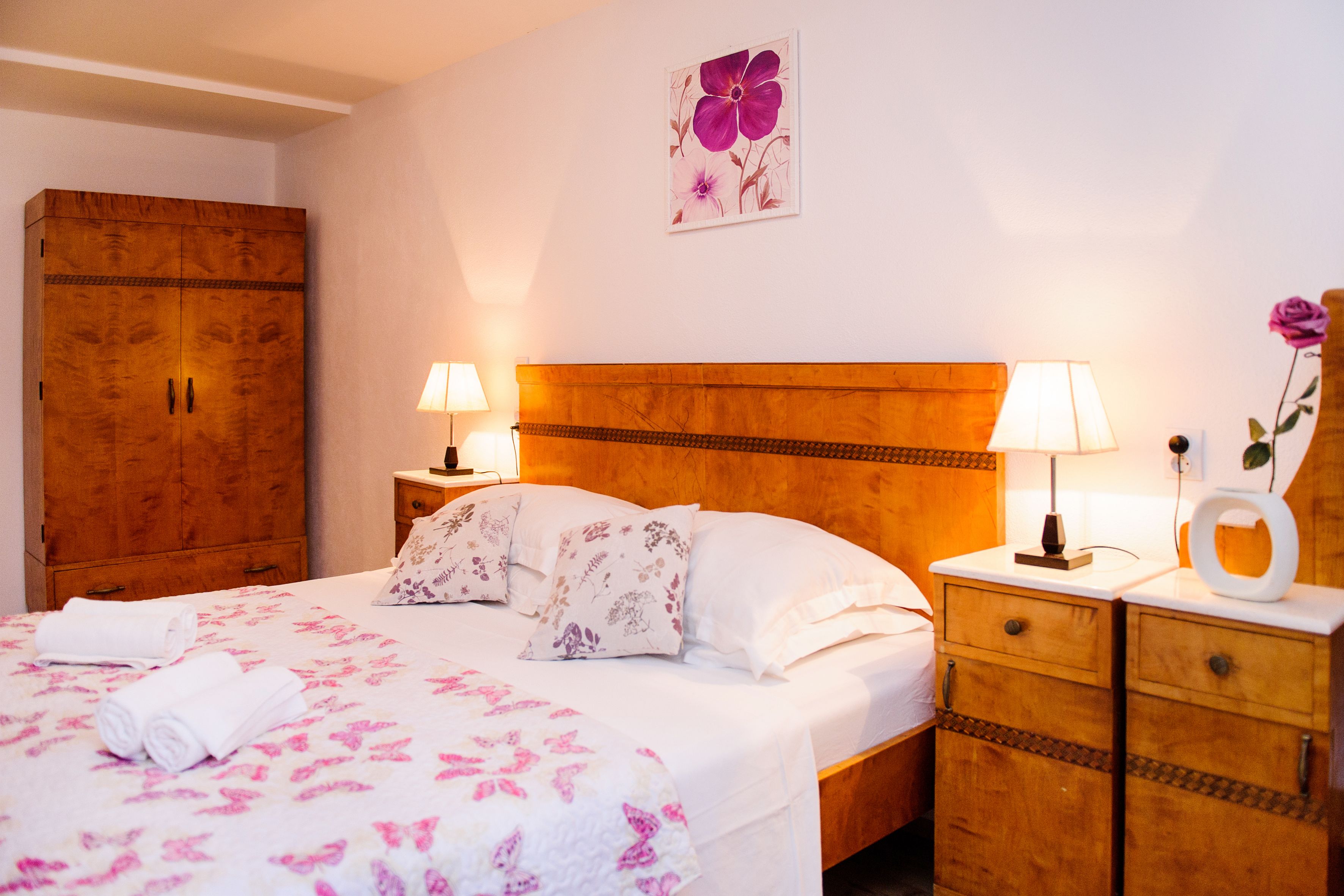 A neatly made bed with floral bedding, a wooden headboard, and bedside lamps.