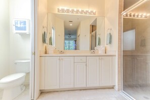 A bathroom with a large mirror, two sinks, and a shower area. - 14543 Abaco Lakes Dr #104 (Cape Coral)