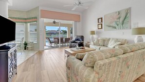A living room with a sofa, a coffee table, and a TV. There is a balcony with a view of the outdoors. - 2318 SE 6th Ave (Cape Coral)