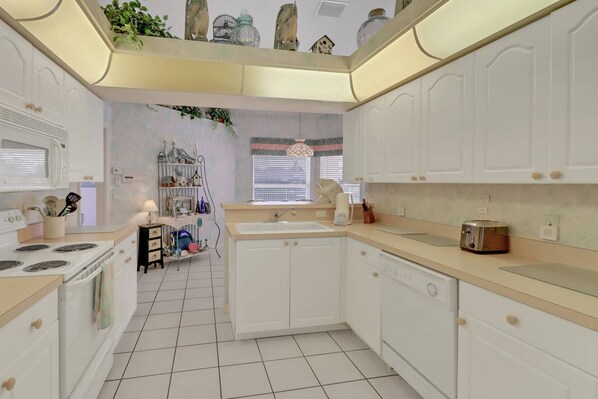 A kitchen with white cabinets, a stove, a sink, and a toaster. There is a window with blinds and a plant on the windowsill.
