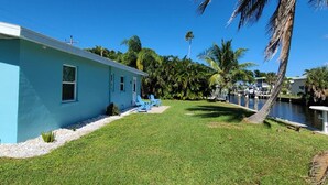 A blue building with a grassy yard, a palm tree, and a body of water. - 16316 Tortuga (Bokeelia)