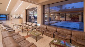 A hotel lobby with leather sofas, a reception desk, and large windows overlooking a street. - Cocoland Yamaguchi Ube (Ube)