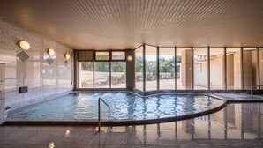 En inomhuspool med kaklade golv och väggar, stora fönster och ett träbeklätt tak.