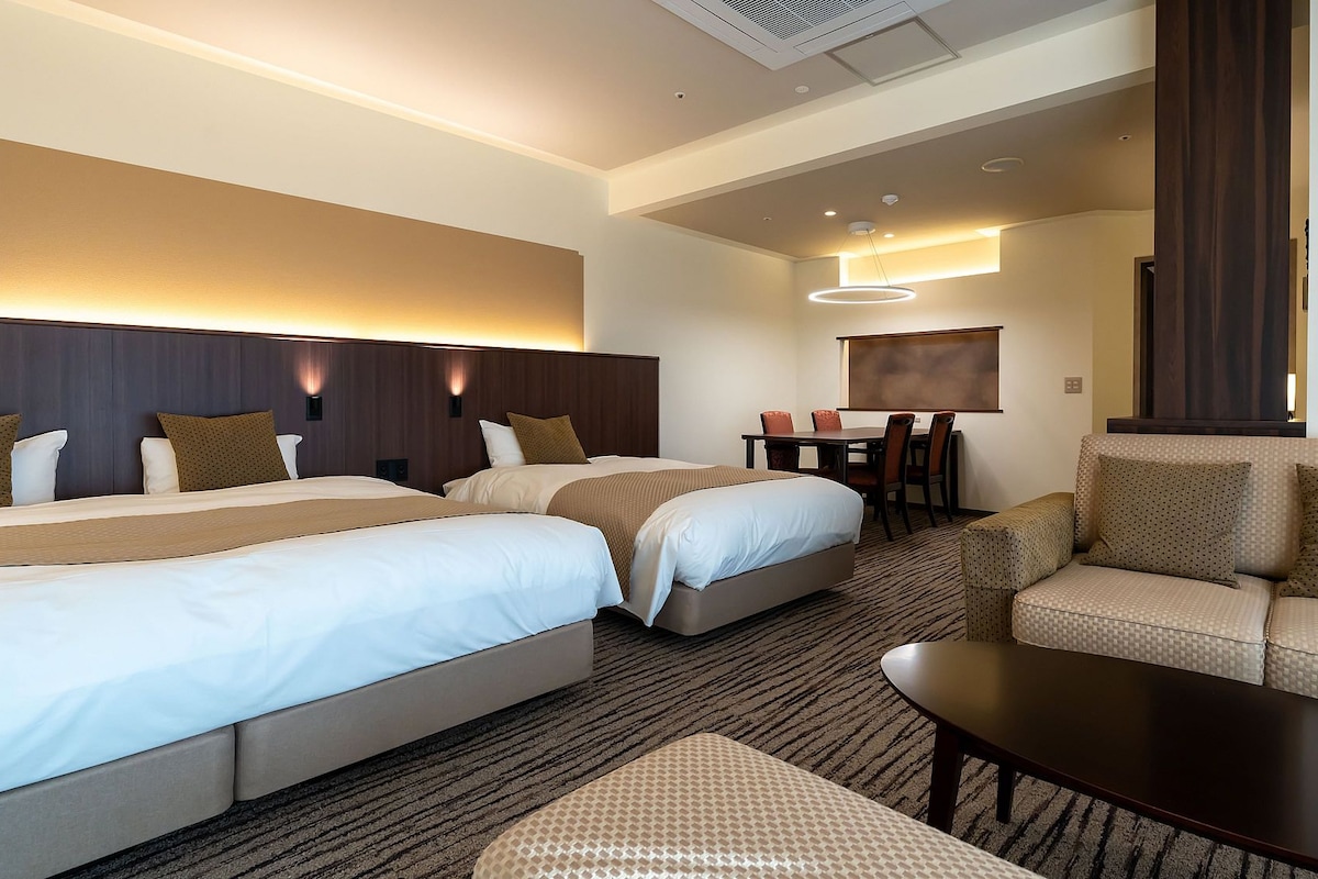 Habitación de hotel con dos camas, un sofá, una mesita y un comedor con sillas.