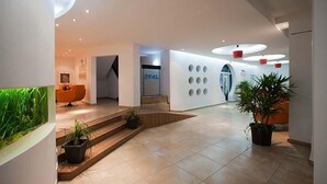 A modern lobby with a reception desk, a staircase, and a wall with circular cutouts. - HOTEL OPAL Cap Aurora (Jupiter)