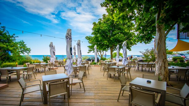 An outdoor patio with tables and chairs, overlooking a body of water. - HOTEL OPAL Cap Aurora (Jupiter)
