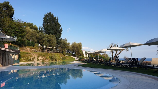 Zona de piscina con sillas de descanso y sombrillas, rodeada de vegetación y un cielo despejado.