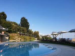 A pool area with lounge chairs and umbrellas, surrounded by greenery and a clear sky. - Domina Borgo degli Ulivi - Lake Garda (Gardone Riviera)