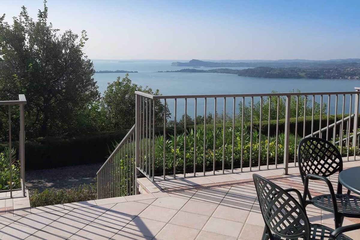Terraza con vistas a una gran extensión de agua, rodeada de vegetación y una barandilla de metal.