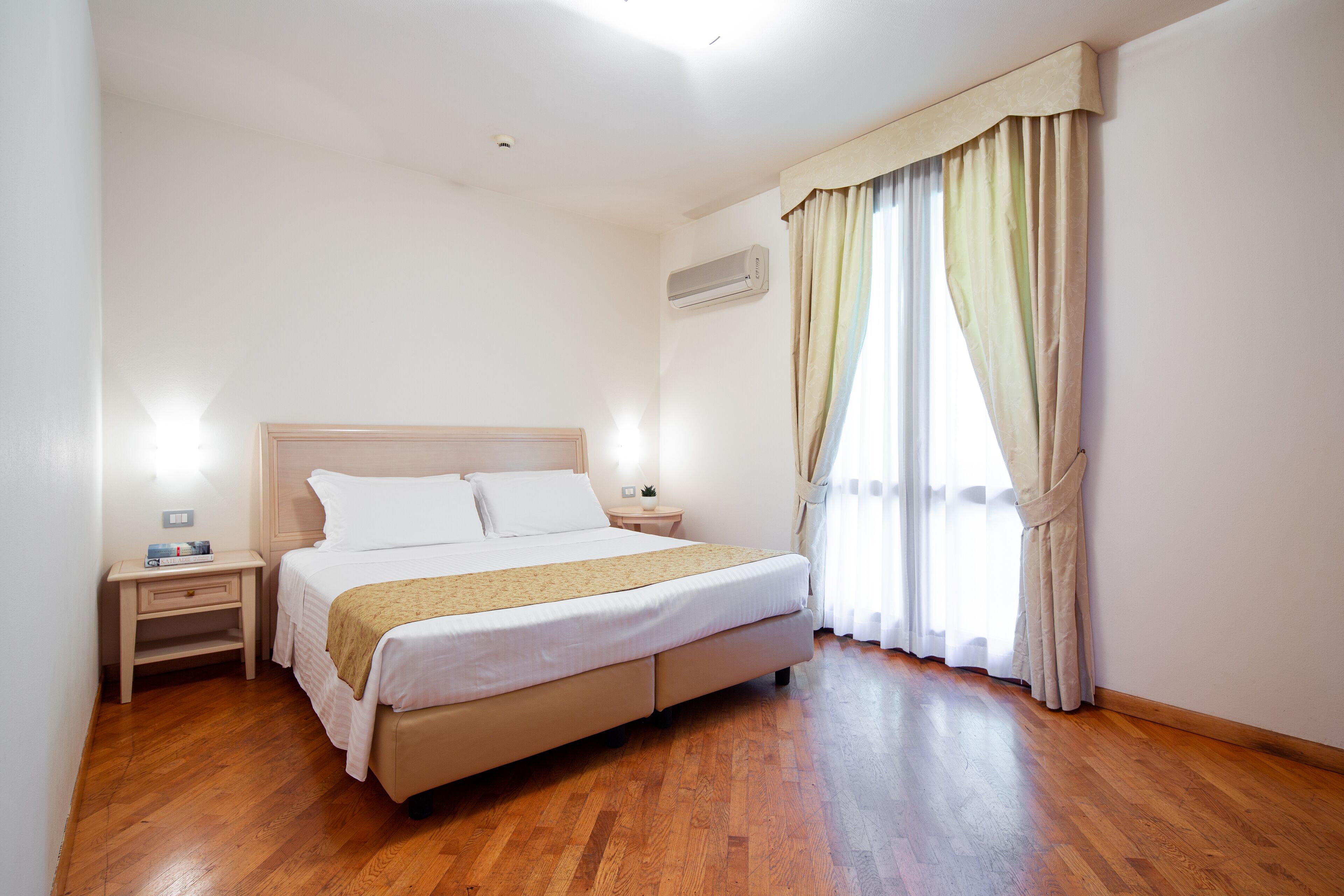 Camera d'albergo con un letto, comodini, un climatizzatore e una finestra con tende.